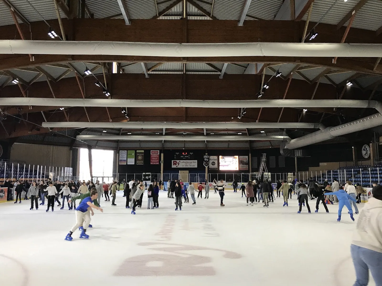 Une séance publique très animée sur la patinoire Arago de La Roche-sur-Yon, des patineurs de tous âges répartis sur la glace sous le toit à fermes en bois. — Patinoire Arago