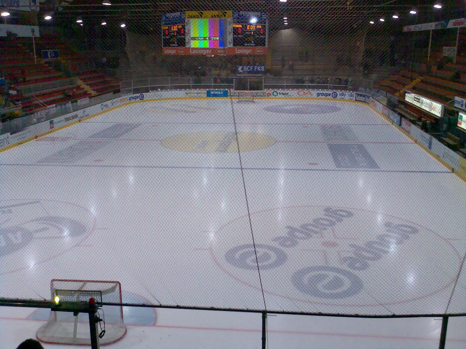 The empty ice of the BCF Arena with its centre-ice and face-off markings, a scoreboard and the stands along one side. — Patinoire BCF Arena