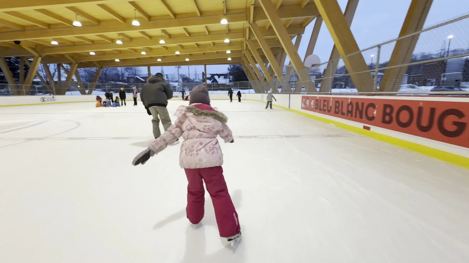 Un niño patinando junto a las vallas rojas Bleu Blanc Bouge de la pista refrigerada techada de Parc Honorine-Melançon, en Saint-Jérôme, visto de espaldas — Patinoire Bleu Blanc Bouge (parc Honorine-Melançon)
