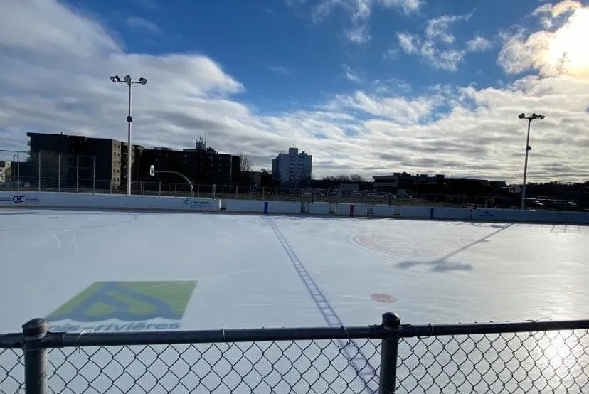 El hielo refrigerado de la pista comunitaria Bleu Blanc Bouge en Trois-Rivières, con la cerca y las luces del parque detrás — Patinoire BLEU BLANC BOUGE