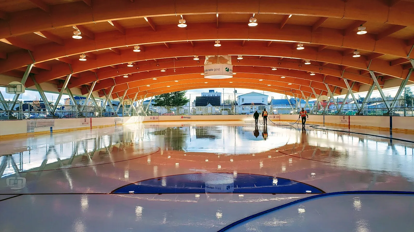 The covered Bleu Blanc Bouge rink in Val-d'Or, with its timber roof and a crew flooding the ice — Patinoire Bleu Blanc Bouge de Val-d'Or