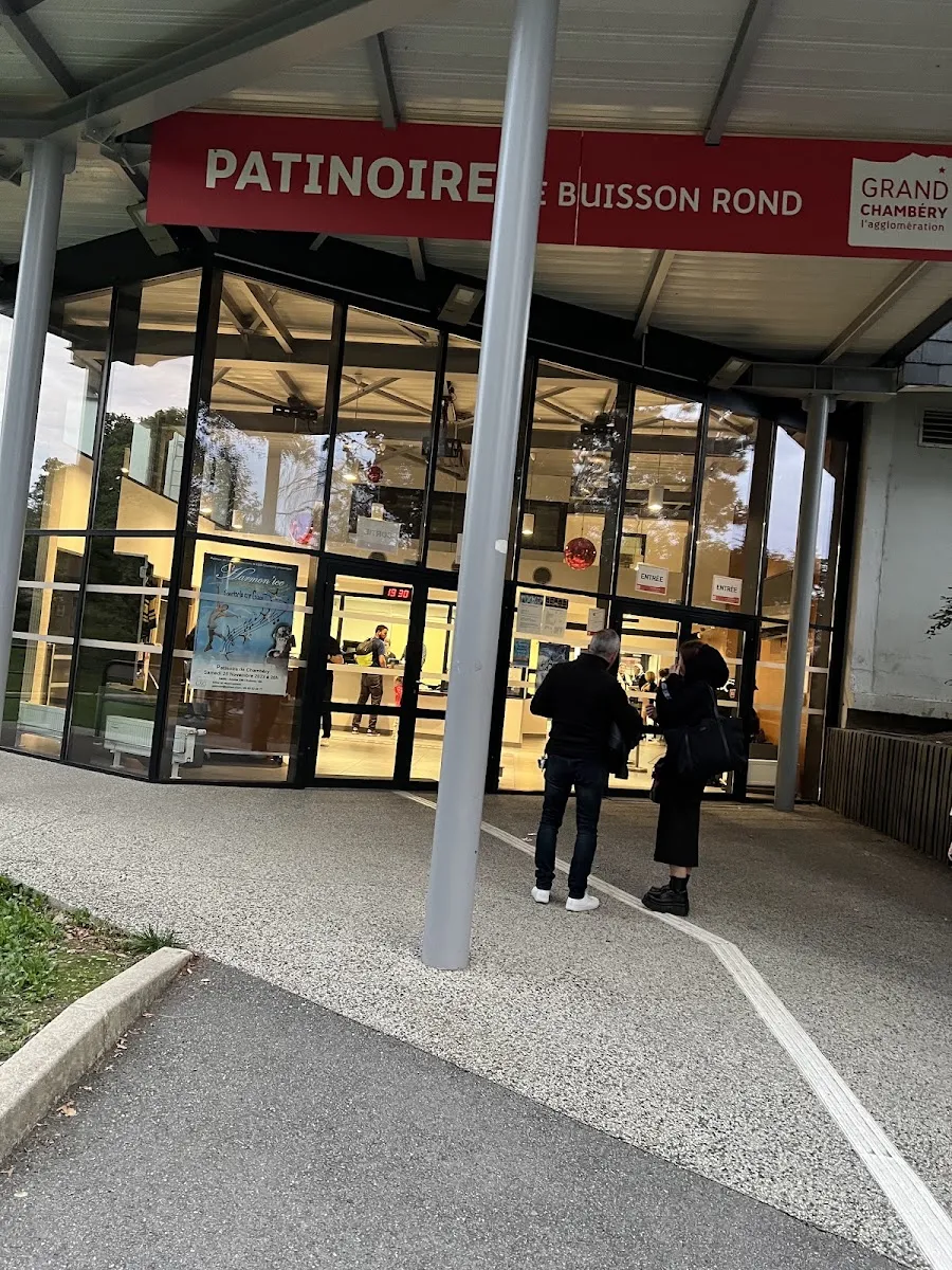 The covered entrance of the Patinoire de Buisson Rond, with its red Patinoire de Buisson Rond sign and the Grand Chambéry logo above the glazed lobby. — Patinoire de Buisson Rond