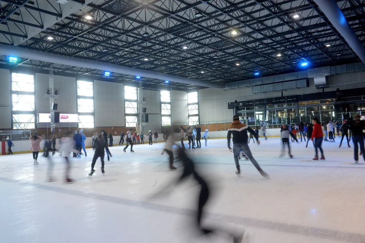 The Buisson Rond hall during a public session, skaters moving across the ice beneath the steel roof and tall windows. — Patinoire de Buisson Rond