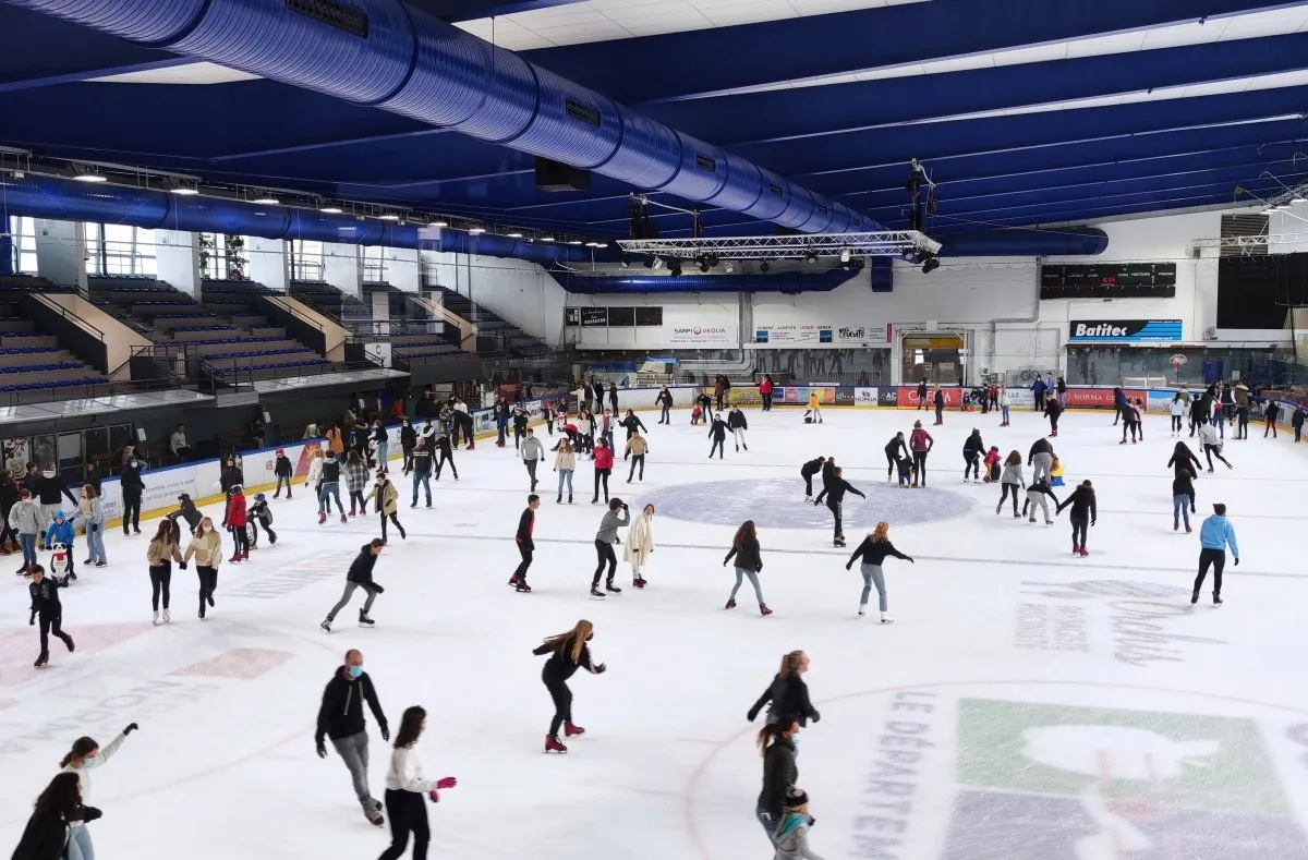 Une séance publique à la patinoire de Caen la mer, des patineurs répartis sur toute la surface sous le toit d’acier bleu, avec les gradins d’un côté. — Patinoire Caen la mer