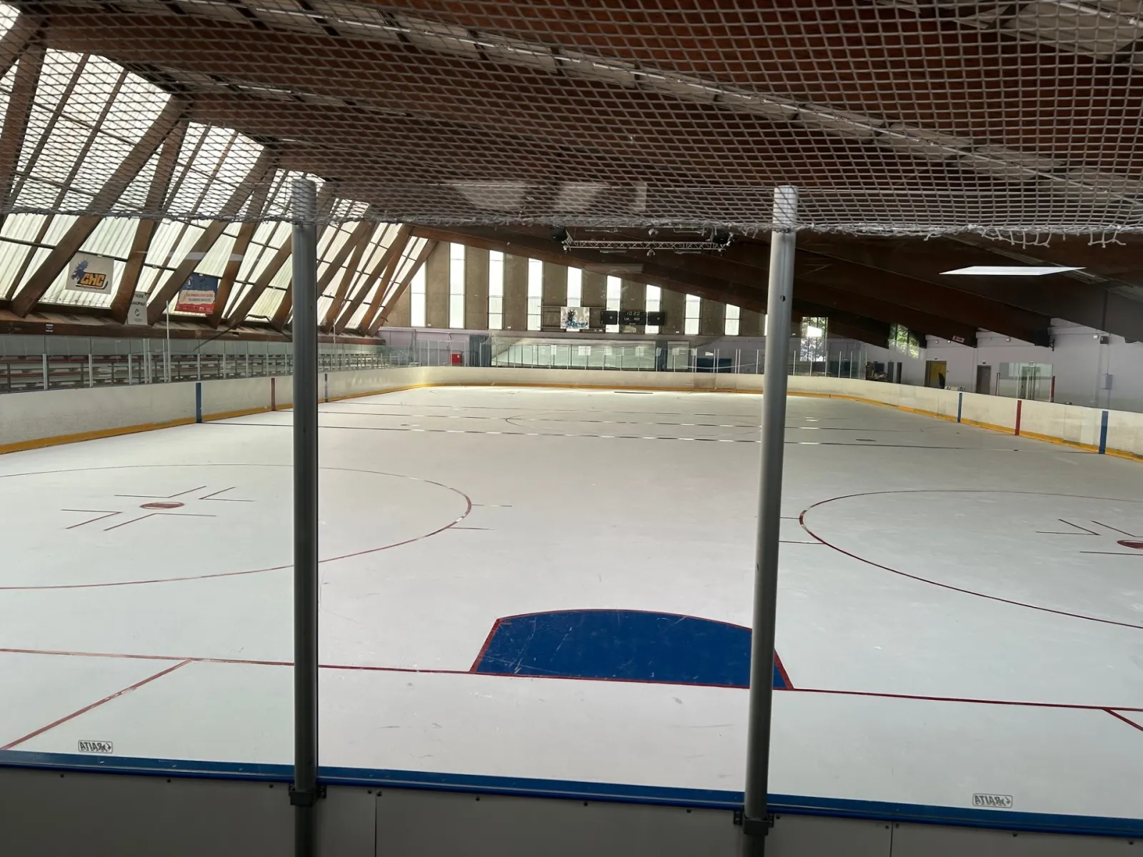 The empty ice sheet seen from behind the glass: hockey markings, boards and a curved timber roof with skylights. — Patinoire de Champigny-sur-Marne