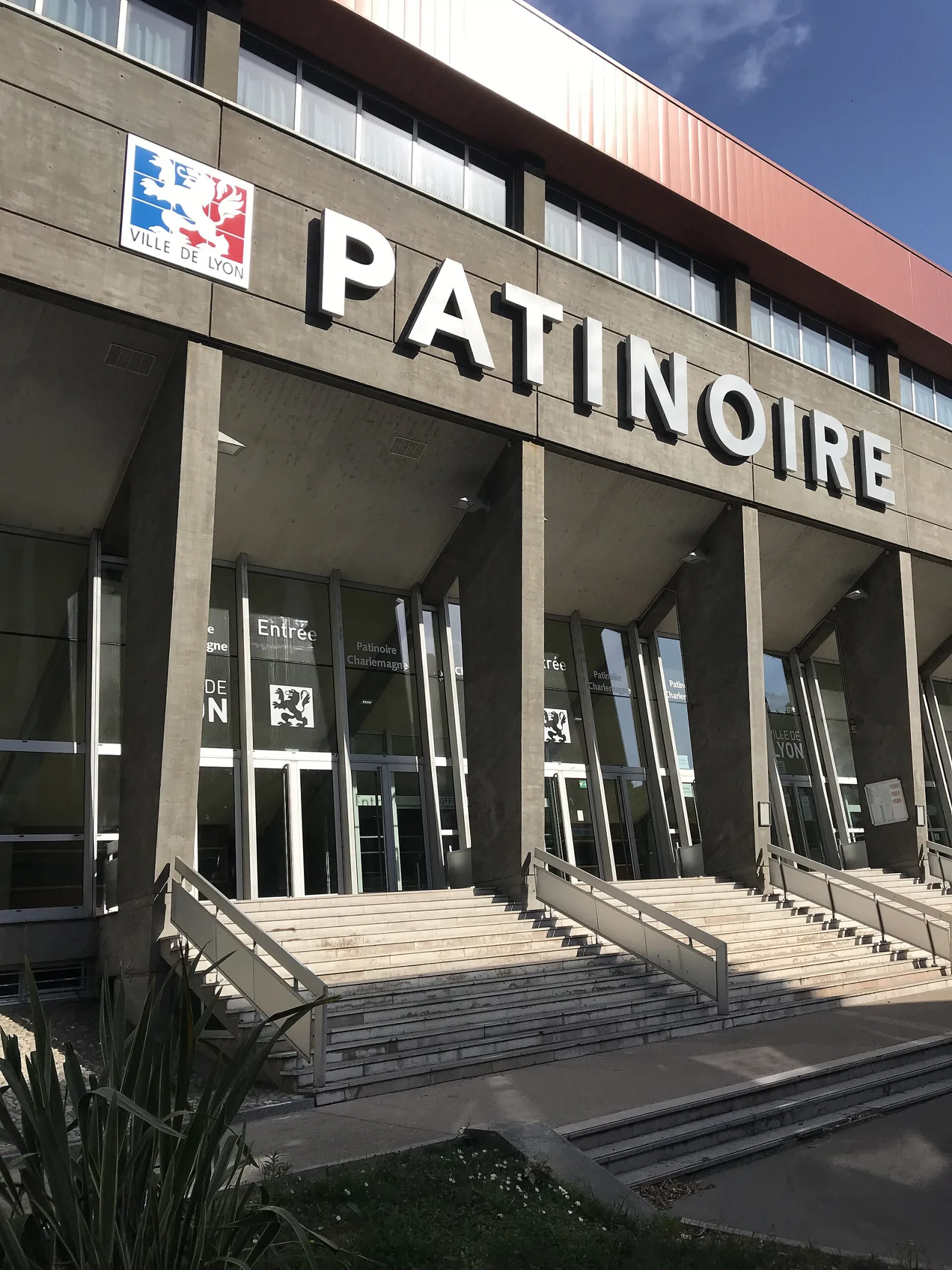 The concrete front of the Charlemagne rink with PATINOIRE lettered across it and the Ville de Lyon arms, above the entrance steps — Patinoire Charlemagne