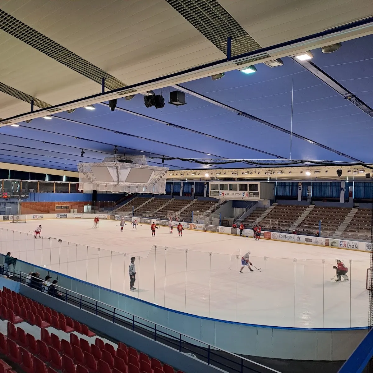 The Charlemagne ice seen from the red stands during a hockey session, under the blue ceiling — Patinoire Charlemagne