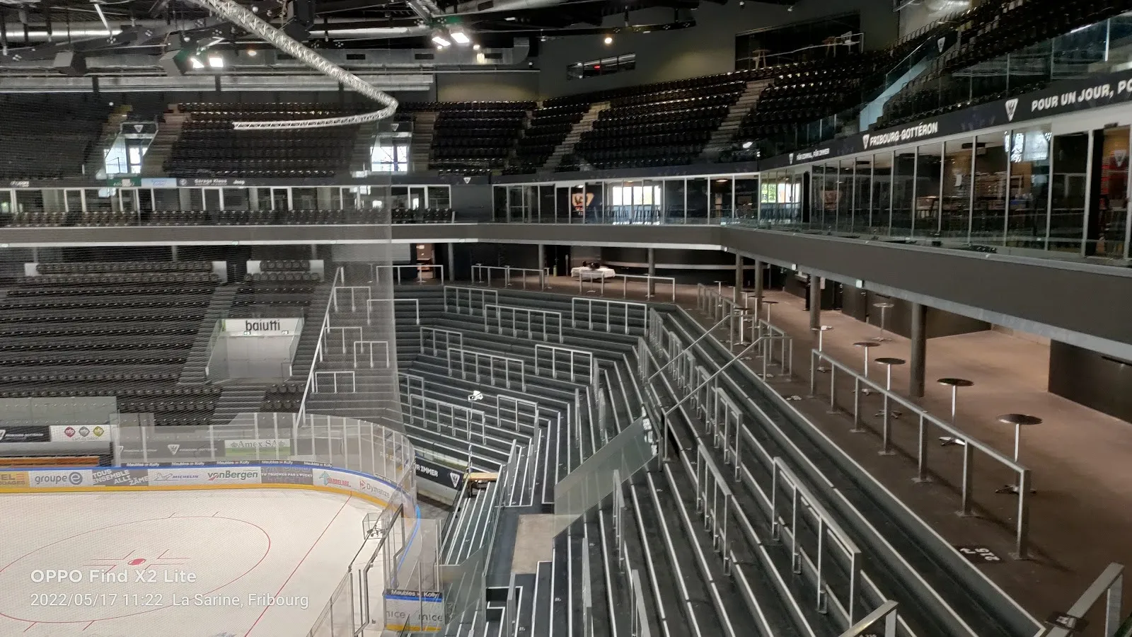 La glace de la patinoire de Saint-Léonard à Fribourg vue depuis les gradins, avec les rangées de sièges, la vitre au-dessus des bandes et la charpente métallique. — Patinoire communale Saint-Léonard