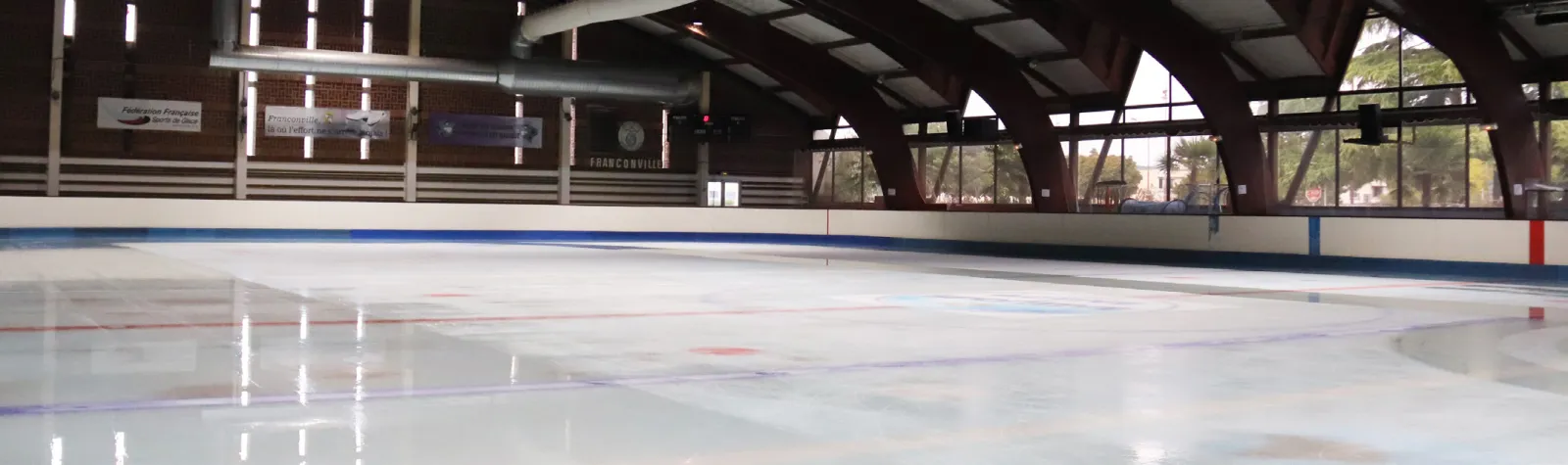 The empty ice of the Franconville rink with its brick end wall, curved timber roof arches and glazed side wall, in the photo printed on page 8 of the town's sports booklet. — Patinoire du CSL