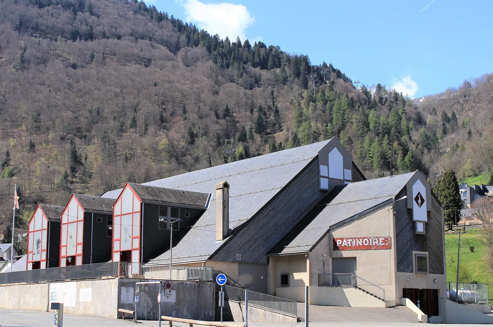 The slate-roofed Patinoire de Cauterets with its red Patinoire sign, stepped gables and the wooded mountainside rising behind. — Patinoire de Cauterets