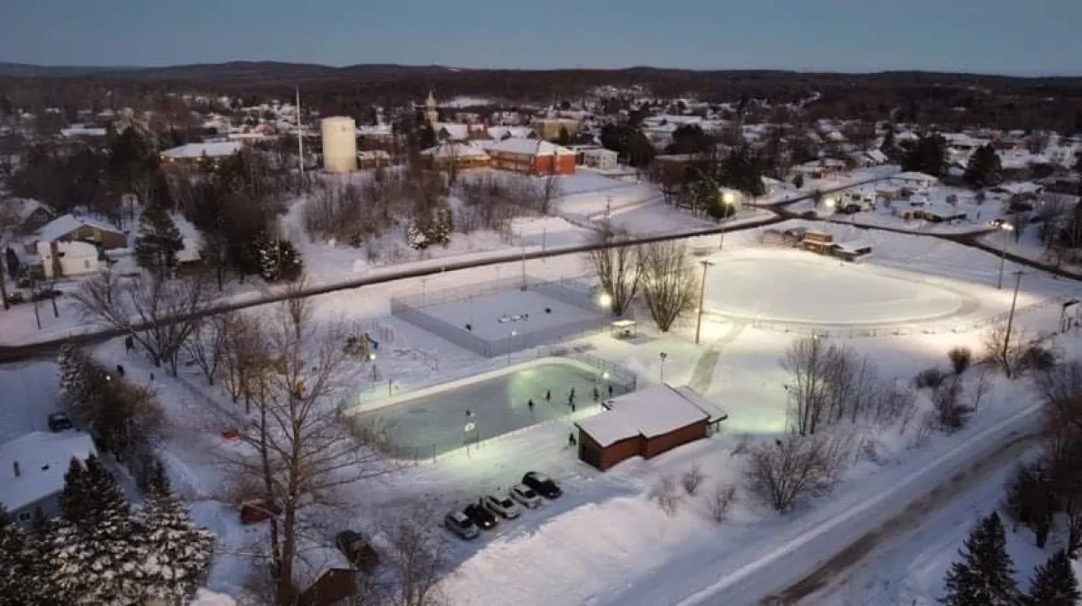 Vue aérienne de nuit du parc Patrick-Gendron à Québec, avec la patinoire de hockey éclairée entre les arbres enneigés et les maisons. — Patinoire de hockey du parc Patrick-Gendron