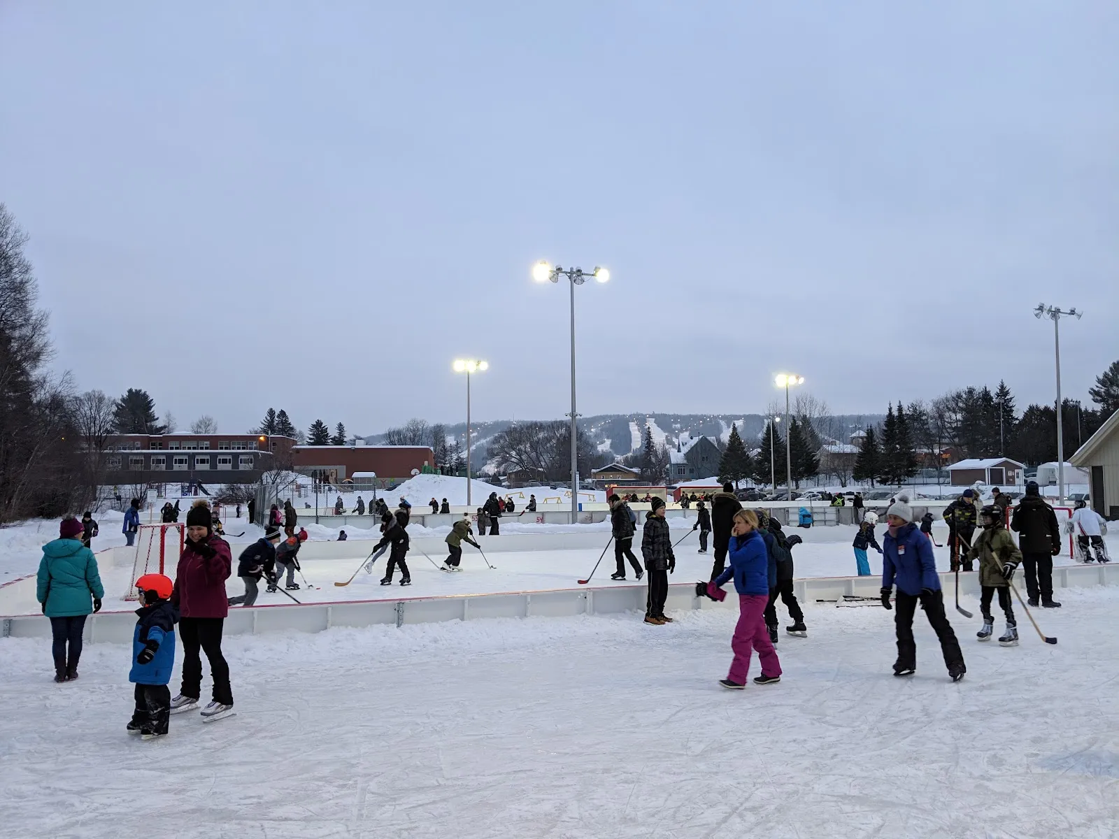Skaters and young hockey players on the outdoor rinks at Parc John-H.-Molson on a winter evening — Patinoire de hockey pour tout-petits du parc John-H.-Molson
