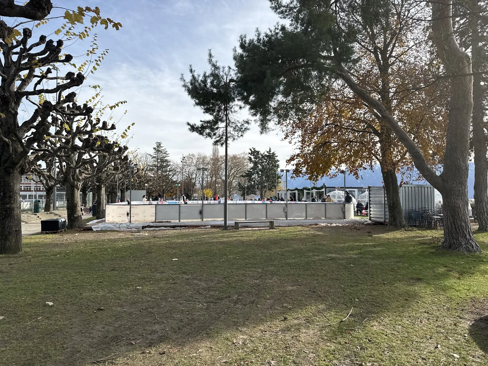 The open-air rink at Lutry among the plane trees by the lake, seen from the park with the boards in the distance — Patinoire de Lutry (Grand-Pont)