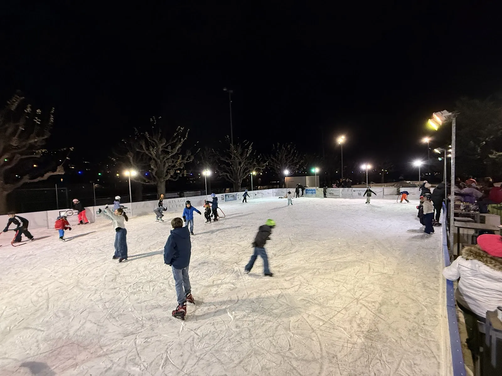 Evening skating on the open-air rink at Lutry under floodlights, skaters of all ages across the sheet — Patinoire de Lutry (Grand-Pont)