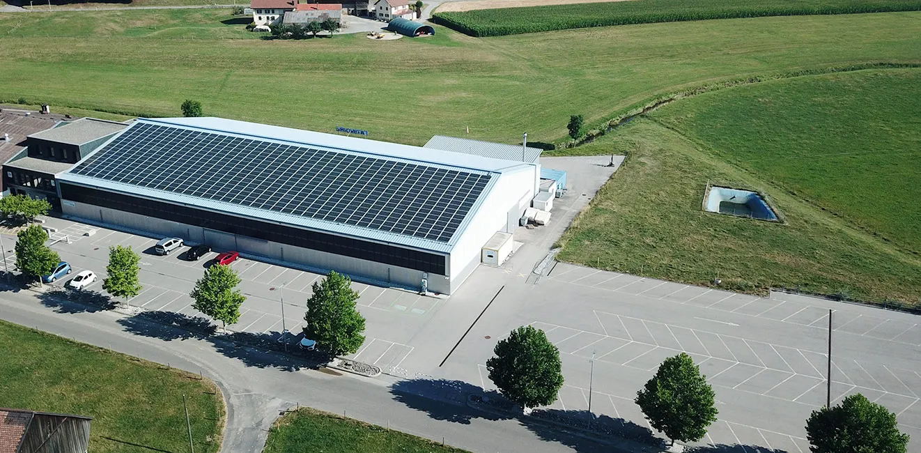 Aerial view of the Romont rink building with its solar roof and car park. — Patinoire de Romont
