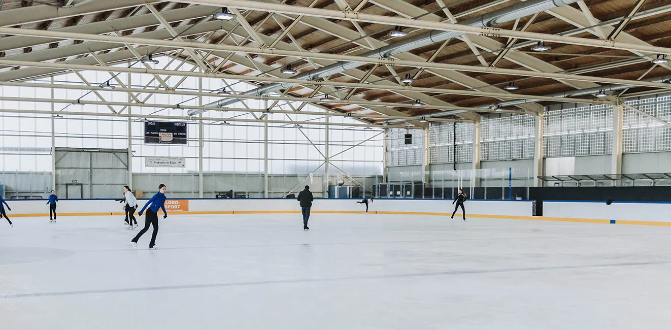 The covered Romont rink with a few skaters at a distance under the timber roof. — Patinoire de Romont
