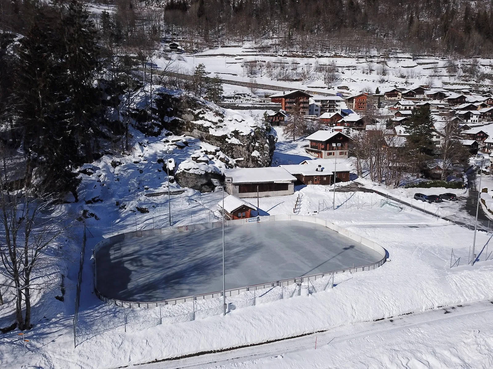 The rink from above in winter, set among chalets and trees at the edge of Salvan village. — Patinoire de Salvan