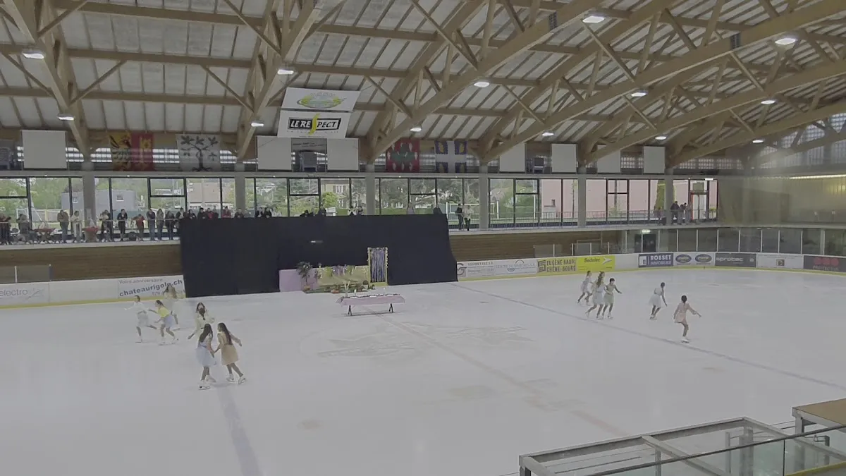 The ice of the Patinoire de Sous-Moulin under its timber roof, with a figure-skating show at the far end — Patinoire de Sous-Moulin