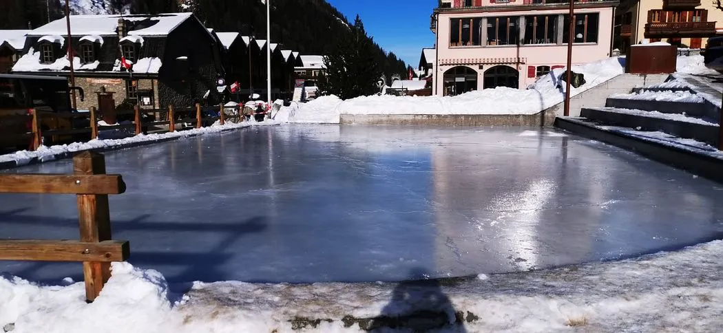 The rink in the village centre with a wooden fence in the foreground, snow banks and chalets behind. — Patinoire de Zinal