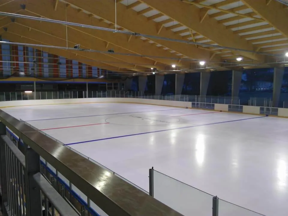The empty ice sheet of the covered Vallorbe rink seen from the gallery, with blue and red lines under the timber roof. — Patinoire des 3 Vallons