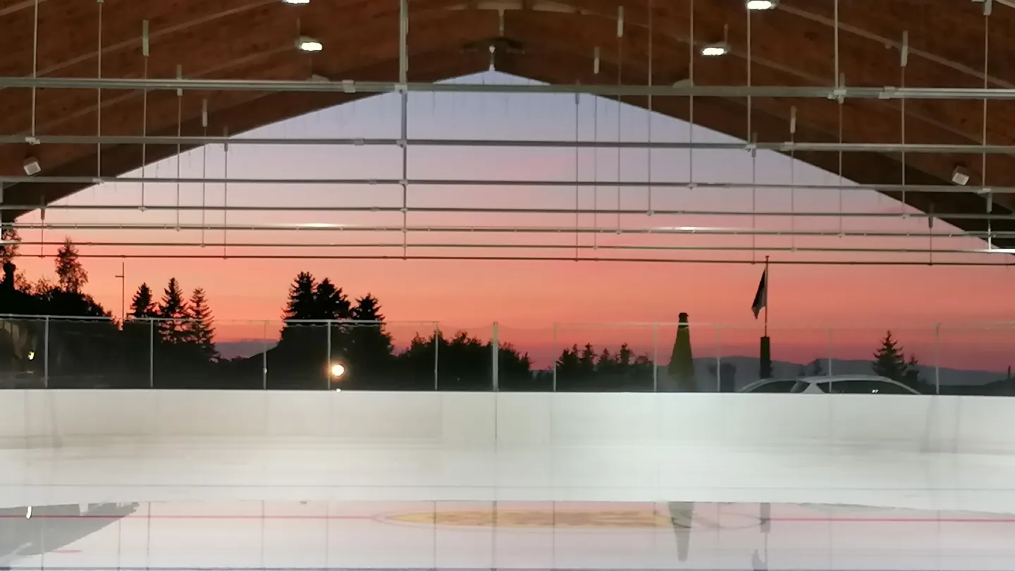 The Paccots rink at dusk with a pink sky glowing at the open end of the arched roof. — Patinoire des Paccots