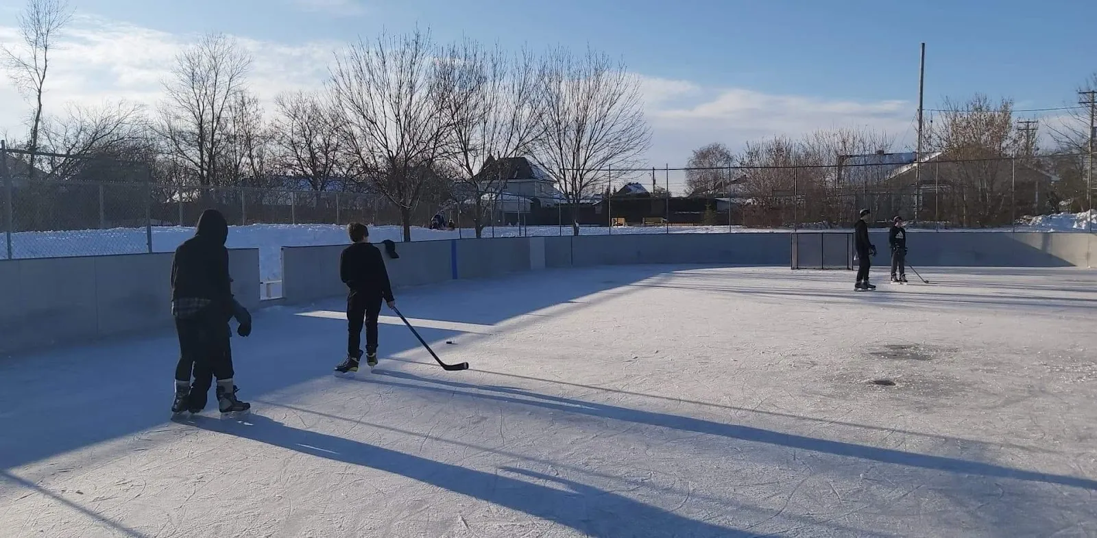 Two hockey players with their backs turned on the boarded outdoor rink at Parc du Mont-Saint-Eustache in winter sun — Patinoire du mont Saint-Eustache