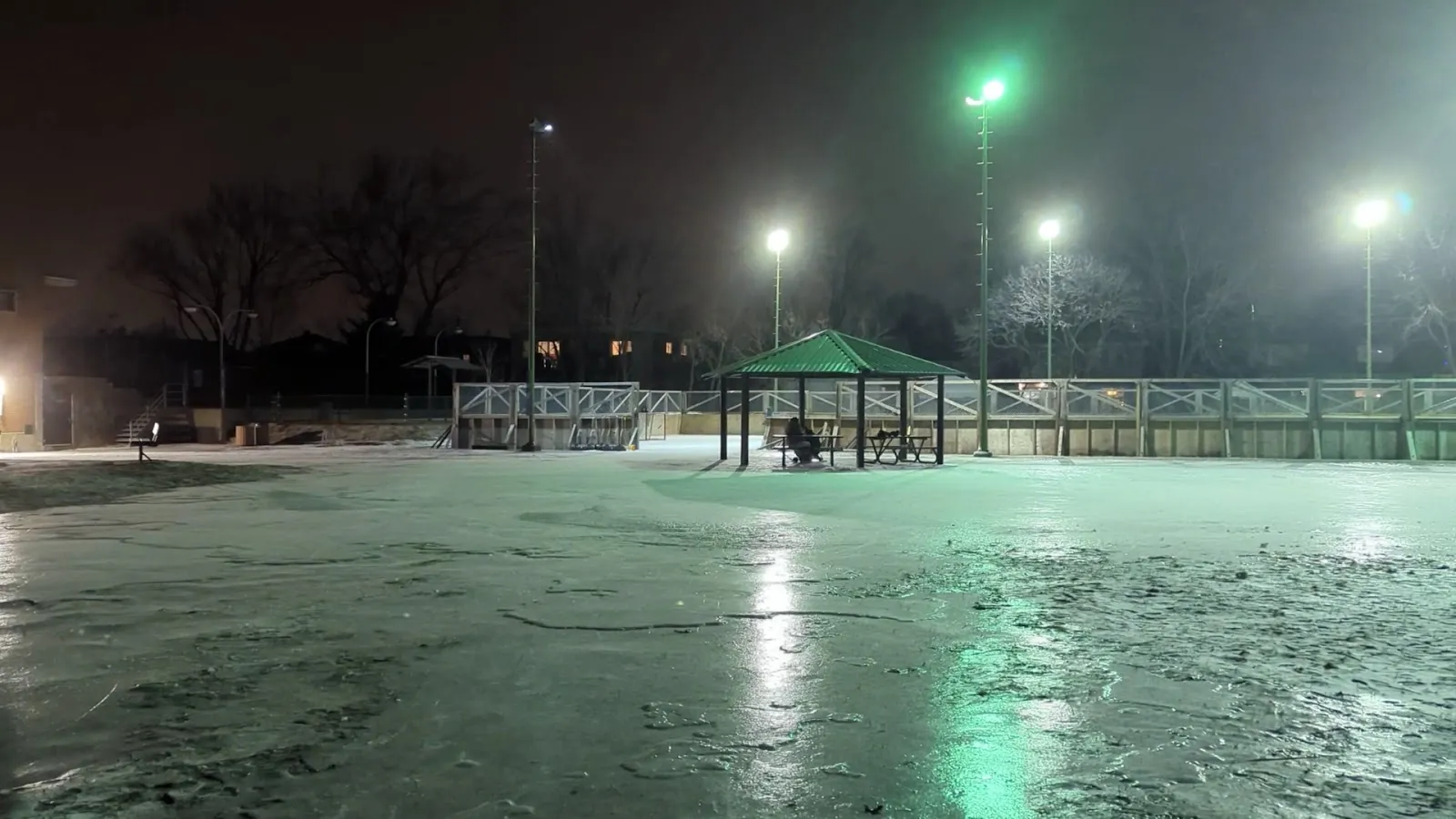 The floodlit rink of the Armand-Racicot park in Longueuil at night, with a green shelter beside the boards — Patinoire du parc Armand-Racicot (Longueuil)