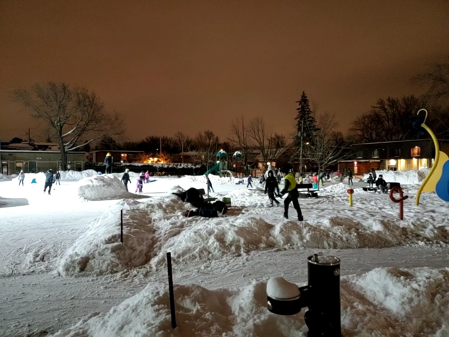 The Armand-Racicot rink at dusk under lamp light with skaters in the distance between snowbanks. — Patinoire du parc Armand-Racicot (Longueuil)