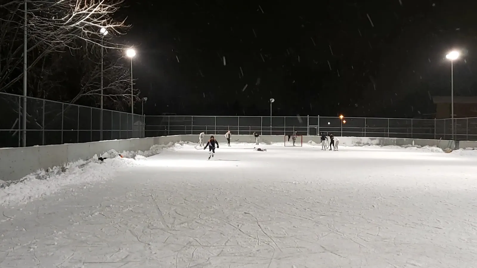 Skaters on the floodlit outdoor rink at Beacon Hill Park on a winter night — Patinoire du parc Beacon Hill (Beaconsfield)