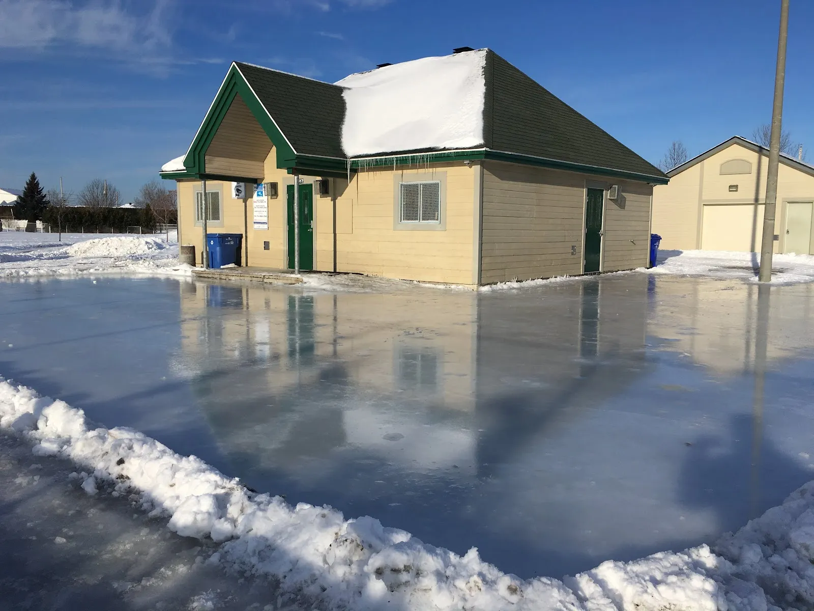 The park chalet at Parc Cardinal in Mirabel standing beside the flooded ice surface, with snowbanks around — Patinoire du parc Cardinal