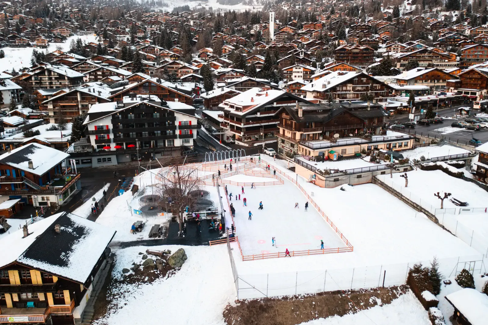 La patinoire de Verbier vue d’en haut : une piste rectangulaire aménagée dans la neige entre les chalets, avec quelques patineurs — Patinoire du Parc de Loisirs (Verbier)
