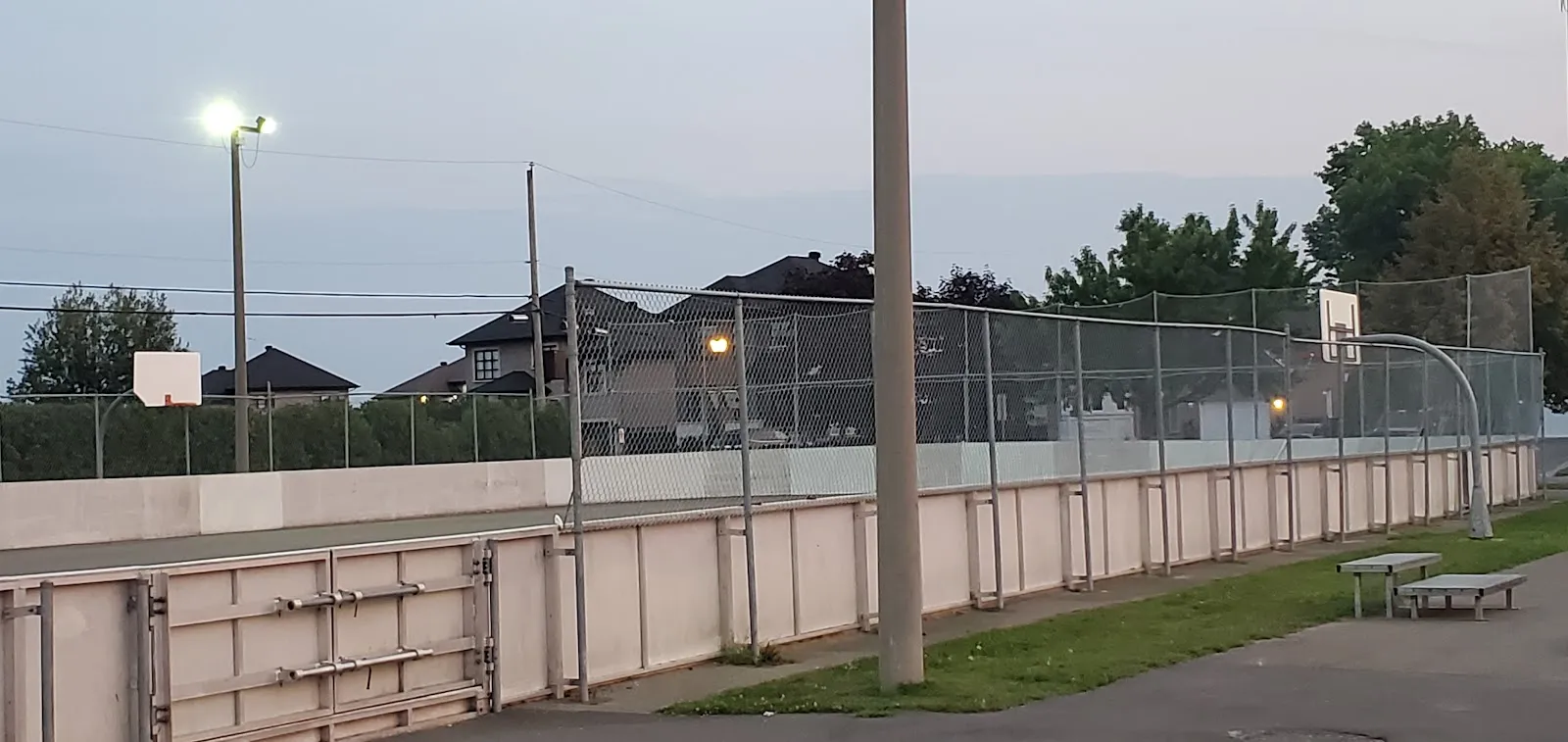 La patinoire multisport avec bandes du parc des Champions à Mirabel vue de l'extérieur en été, avec des projecteurs et un panier de basketball, sans glace — Patinoire du parc des Champions