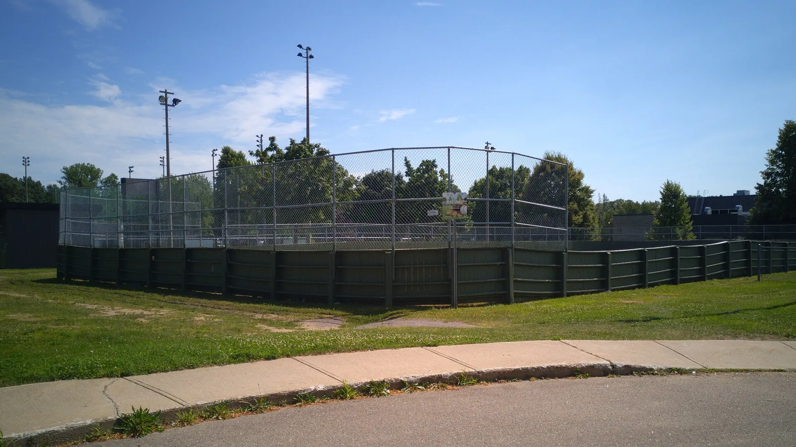 The boarded outdoor rink at Parc des Seigneurs in Trois-Rivières, seen from the street in summer. — Patinoire du parc des Seigneurs