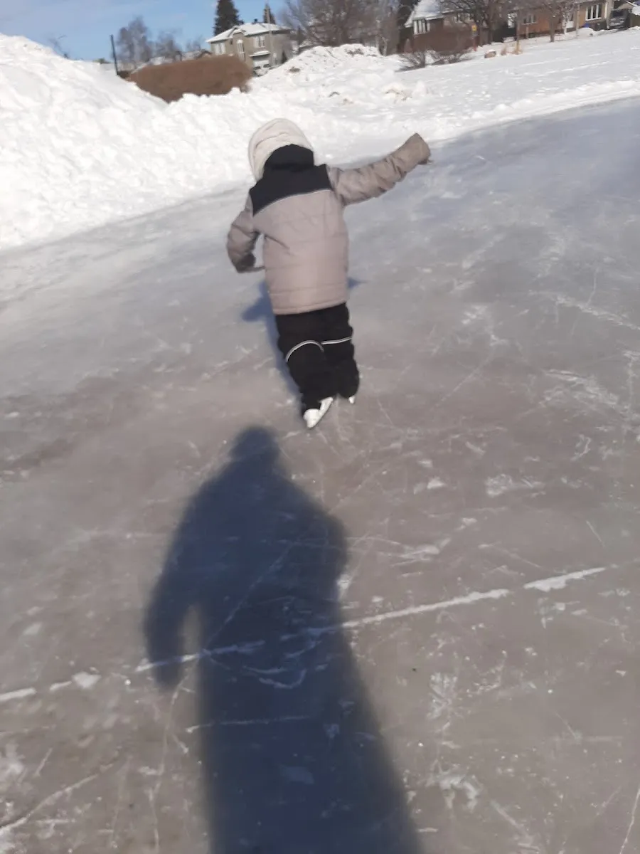 Un enfant patine, vu de dos, sur la glace extérieure du parc du Moulin à Repentigny, avec des bancs de neige et des maisons au loin — Patinoire du parc du Moulin