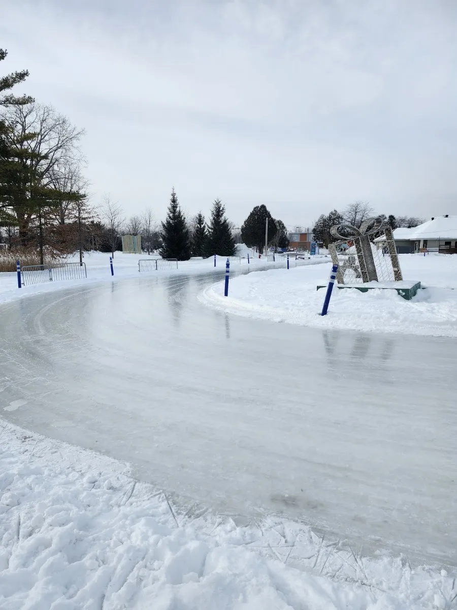 Le sentier glacé sinueux du parc équestre de Blainville en hiver, bordé de poteaux bleus et de bancs de neige, avec une sculpture en forme de cadeau festive à côté — Patinoire du parc équestre