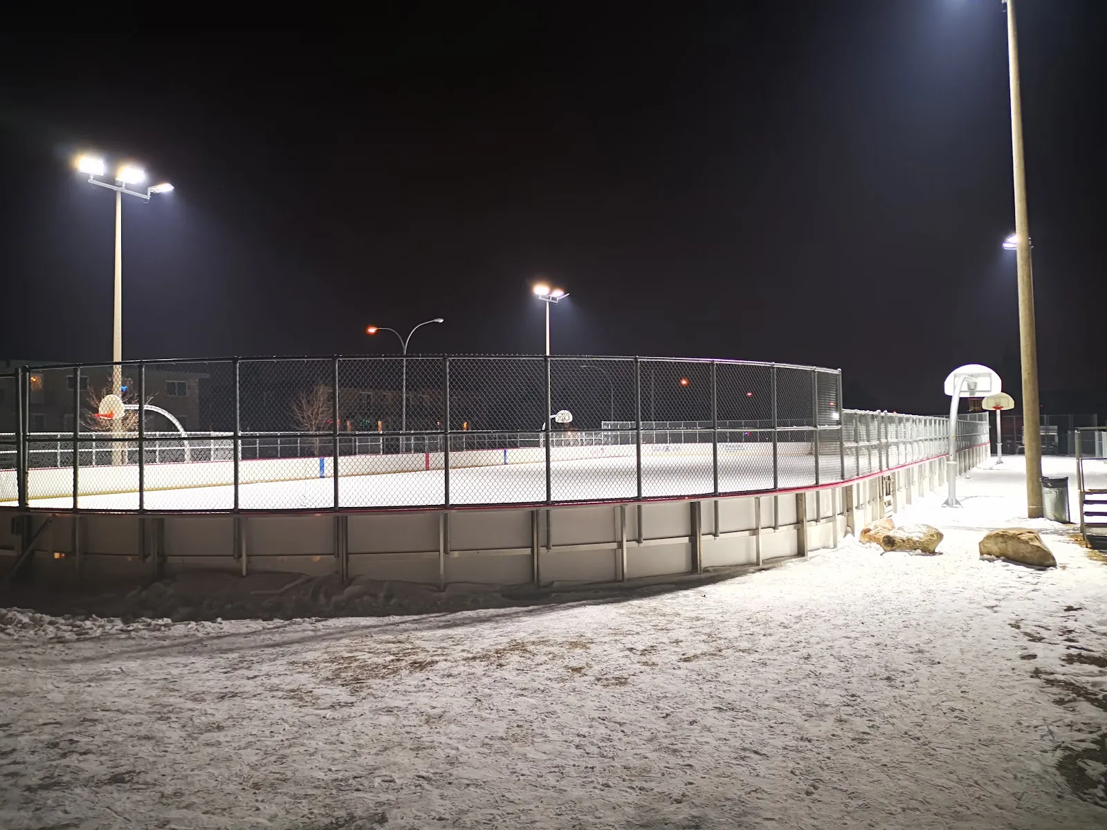 The fenced, floodlit rink at Parc Lionel-Groulx at night, with the boards and basketball hoops beside it — Patinoire du parc Lionel-Groulx (Longueuil)