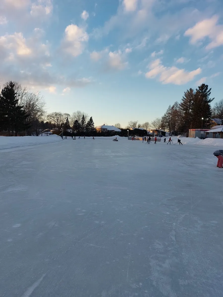 Skaters far across the wide natural ice of the lake rink at Parc Meilleur in Mirabel under an evening sky — Patinoire du parc Lucien-Meilleur