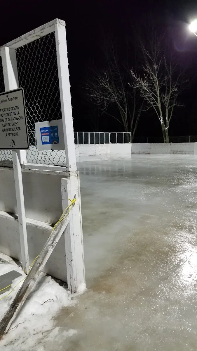 The empty boarded outdoor rink at Parc Nordic at night, with white boards, a net and glossy ice under the floodlights. — Patinoire du parc Nordic
