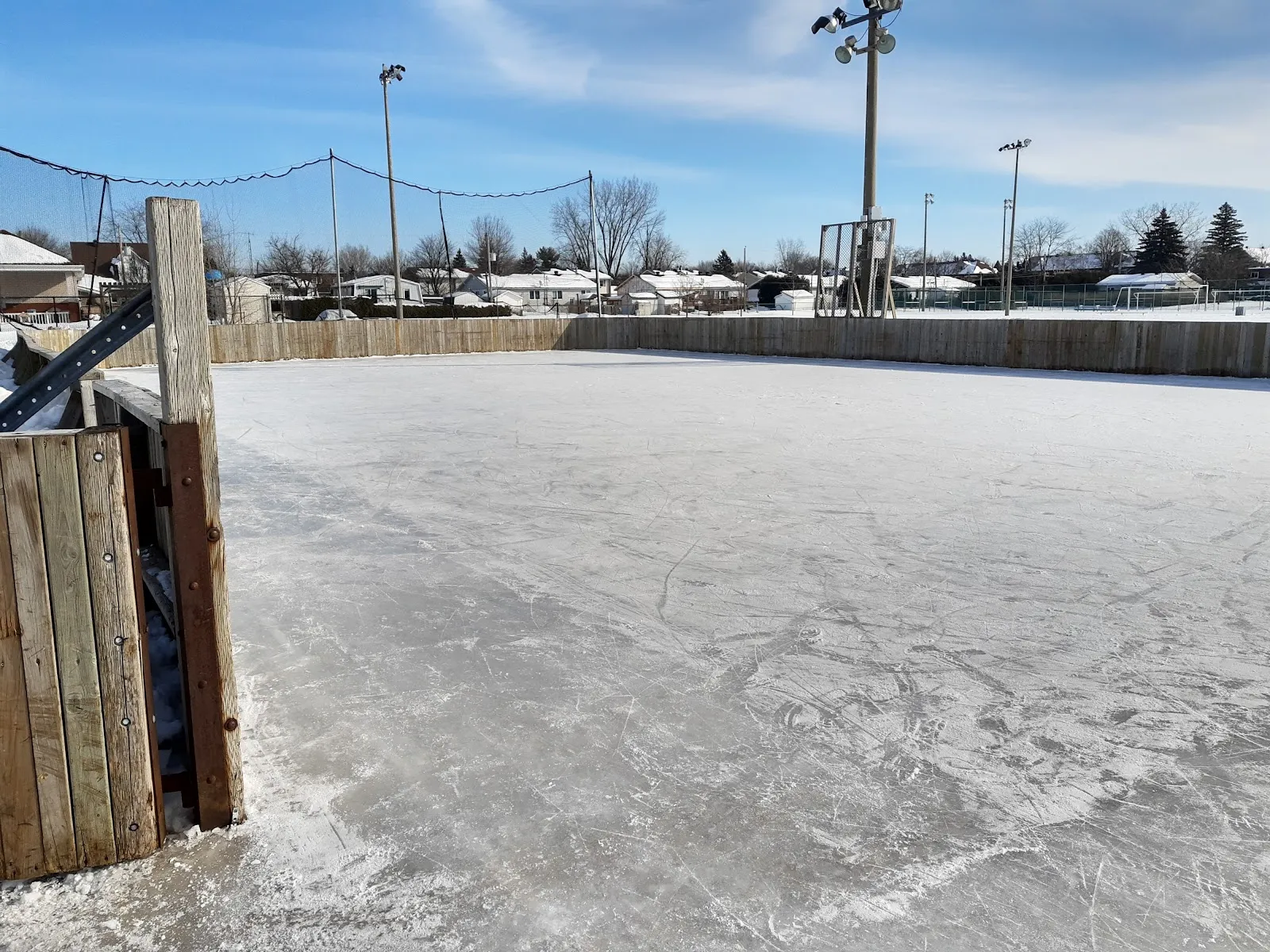 La patinoire extérieure vide du parc Pellerin à Boisbriand par une journée d'hiver dégagée, avec ses bandes en bois, ses projecteurs et des maisons voisines — Patinoire du parc Pellerin