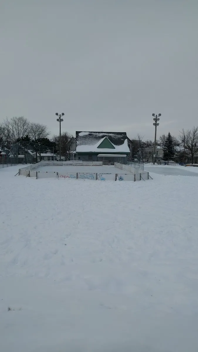 The boarded neighbourhood rink at Parc Sainte-Bernadette under a snow cover, with the warming shelter and floodlights behind. — Patinoire du parc Sainte-Bernadette (Gatineau)