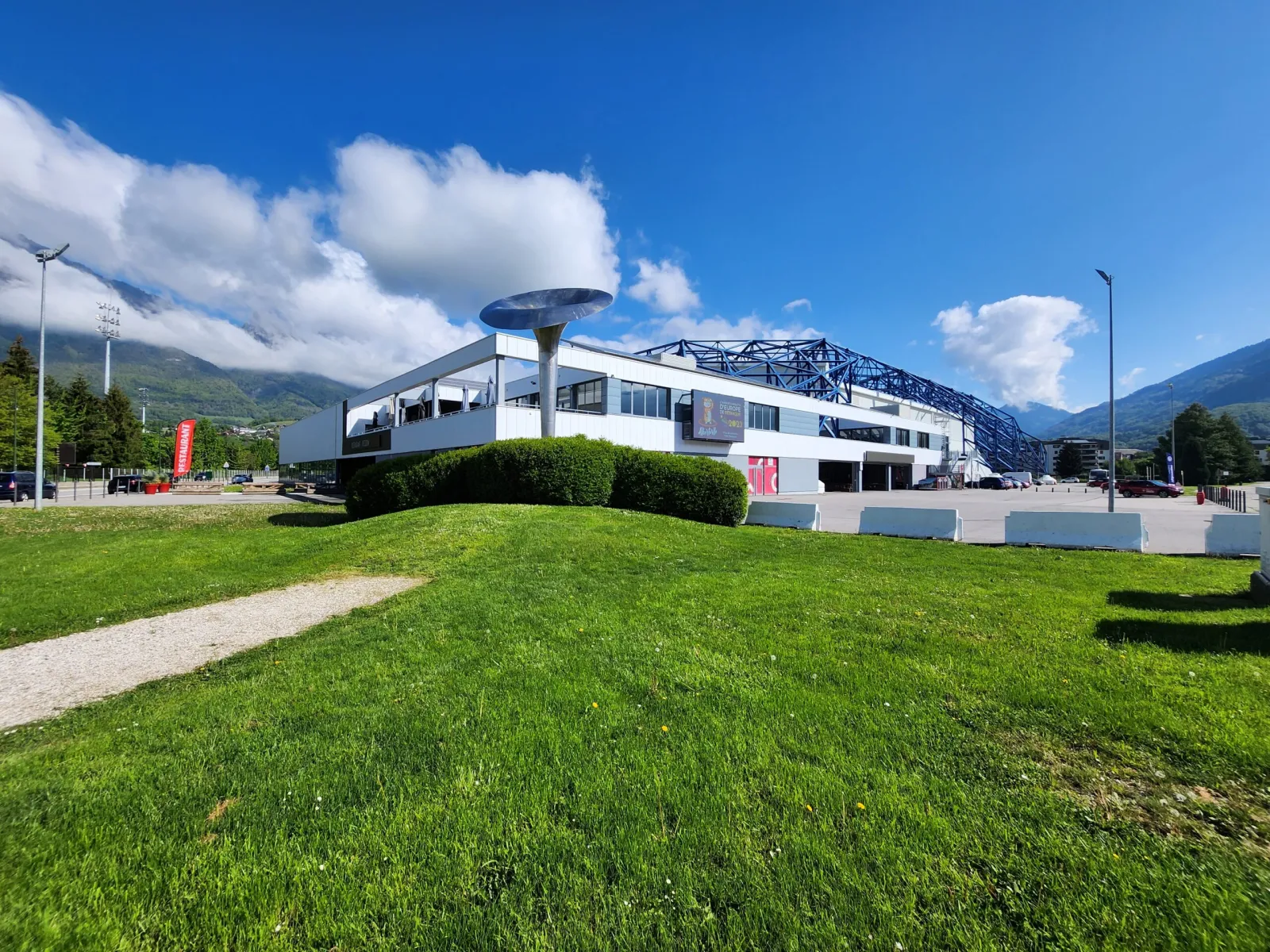 The Halle Olympique d'Albertville seen across the grass with the mountains behind — Patinoire de la Halle Olympique