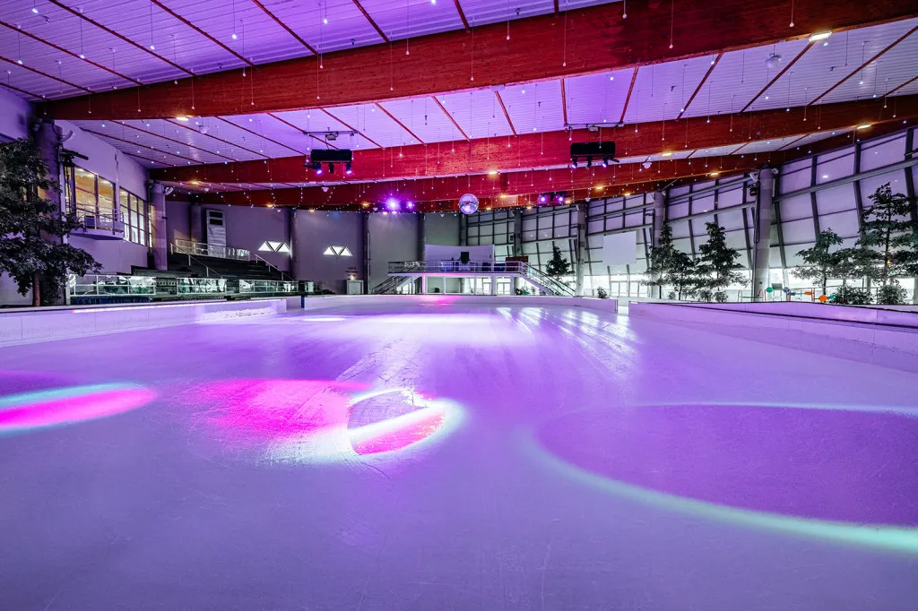The 1,200 m² ice pad of the Hélicéa rink under coloured lights — Patinoire Hélicéa