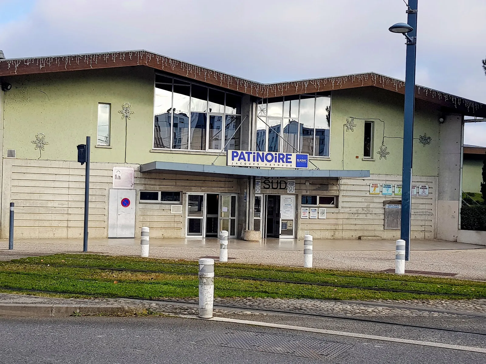 The patinoire's low entrance building with the Patinoire sign over the glazed lobby, seen across the tram tracks. — Patinoire Jacques Raynaud