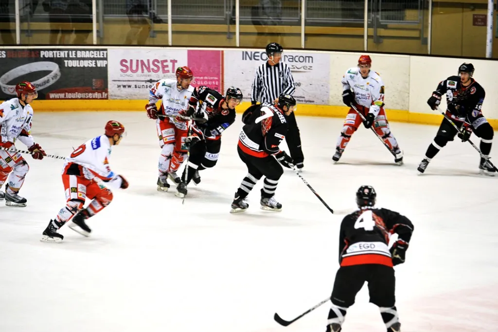 An ice hockey game in play on the Blagnac rink, players from both teams chasing the puck along the boards. — Patinoire Jacques Raynaud