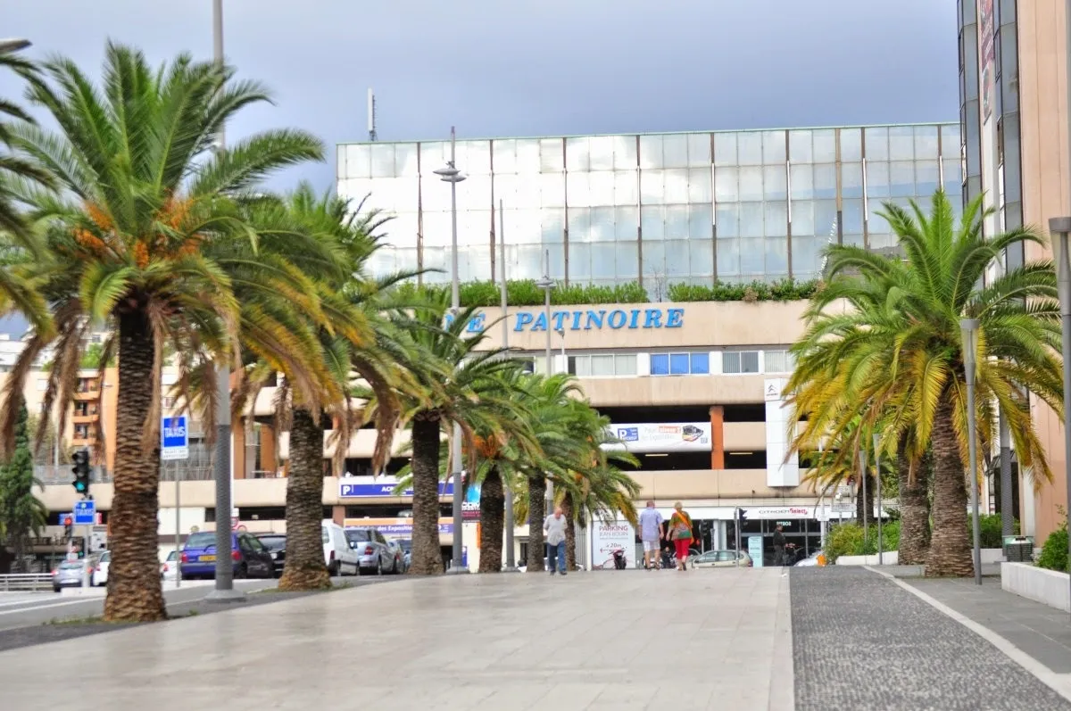 Le Palais des sports Jean-Bouin, à façade vitrée, à Nice, vu entre des palmiers, avec l’enseigne PATINOIRE au-dessus de l’entrée. — Patinoire Jean Bouin