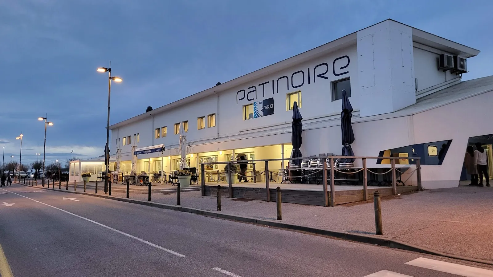 Vue côté rue de la patinoire de la Barre à Anglet au crépuscule, avec l’enseigne PATINOIRE sur le bâtiment blanc. — Patinoire de la Barre
