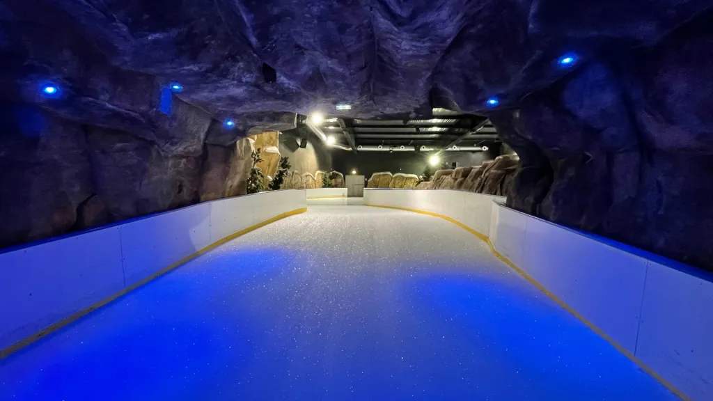 The empty ice rink at La Bulle inside a rock-cave setting with a blue-lit ceiling and white boards curving away down the length of the ice. — Patinoire de La Bulle (Saint-Quentin)
