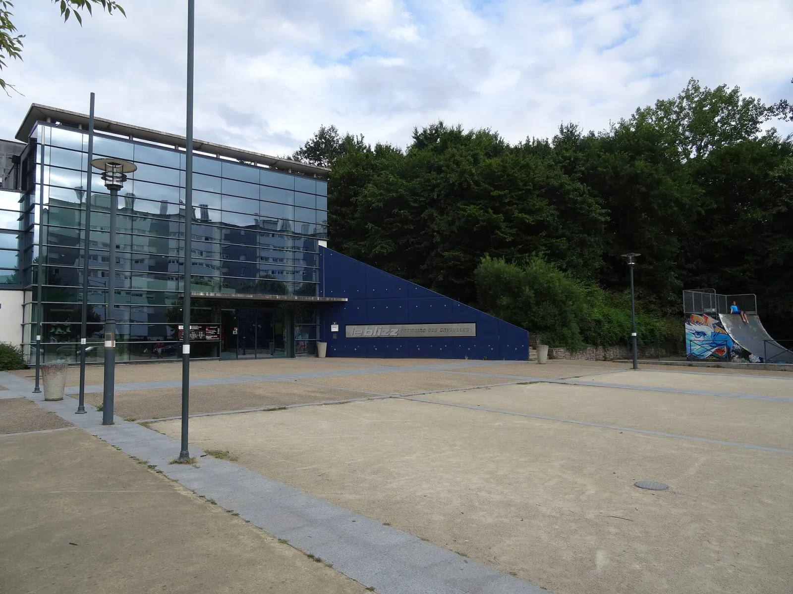 The glazed entrance block and blue wall of Le Blizz on the Gayeulles park side, with the rink's name lettered on the wall — Le Blizz