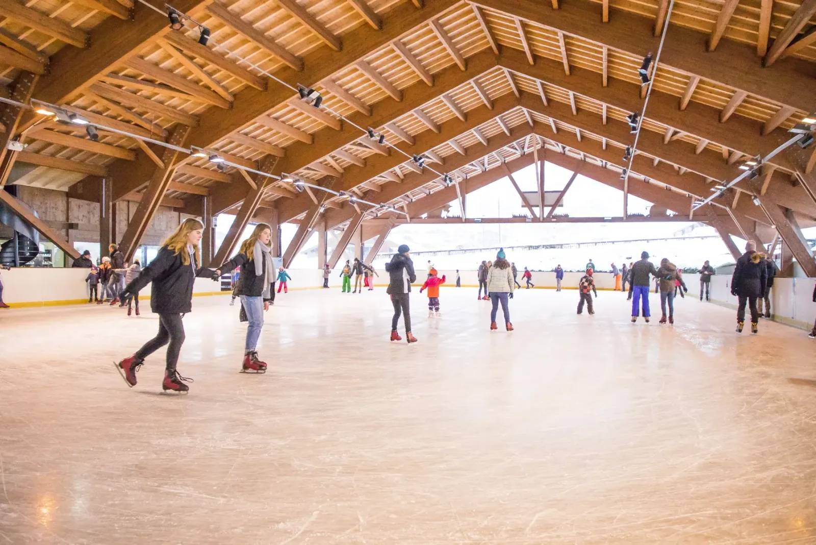 La glace couverte de la patinoire du Grand-Bornand sous sa charpente en bois, avec des patineurs sur la glace. — Patinoire du Grand-Bornand