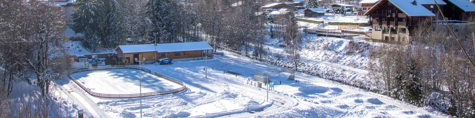 Vue aérienne de la patinoire de plein air parmi des chalets et des arbres enneigés aux Loyers, aux Contamines-Montjoie. — Patinoire Jean-Christophe Simond (Les Contamines-Montjoie)